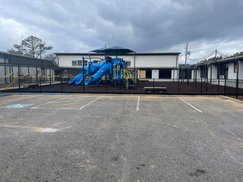 Playground behind a black fence, blue slide, and building under a cloudy sky. Yellow caution tape present.