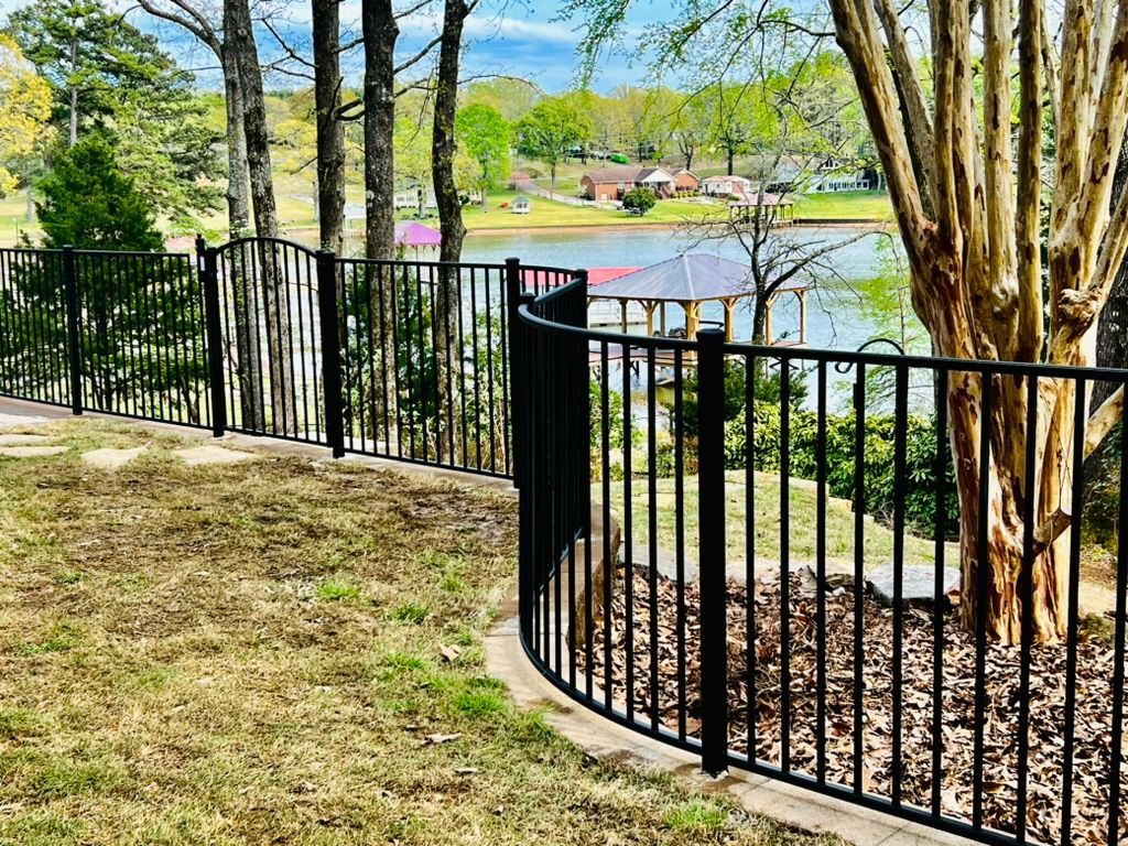 Black metal fence curves around a yard, with a lake and trees visible in the background.