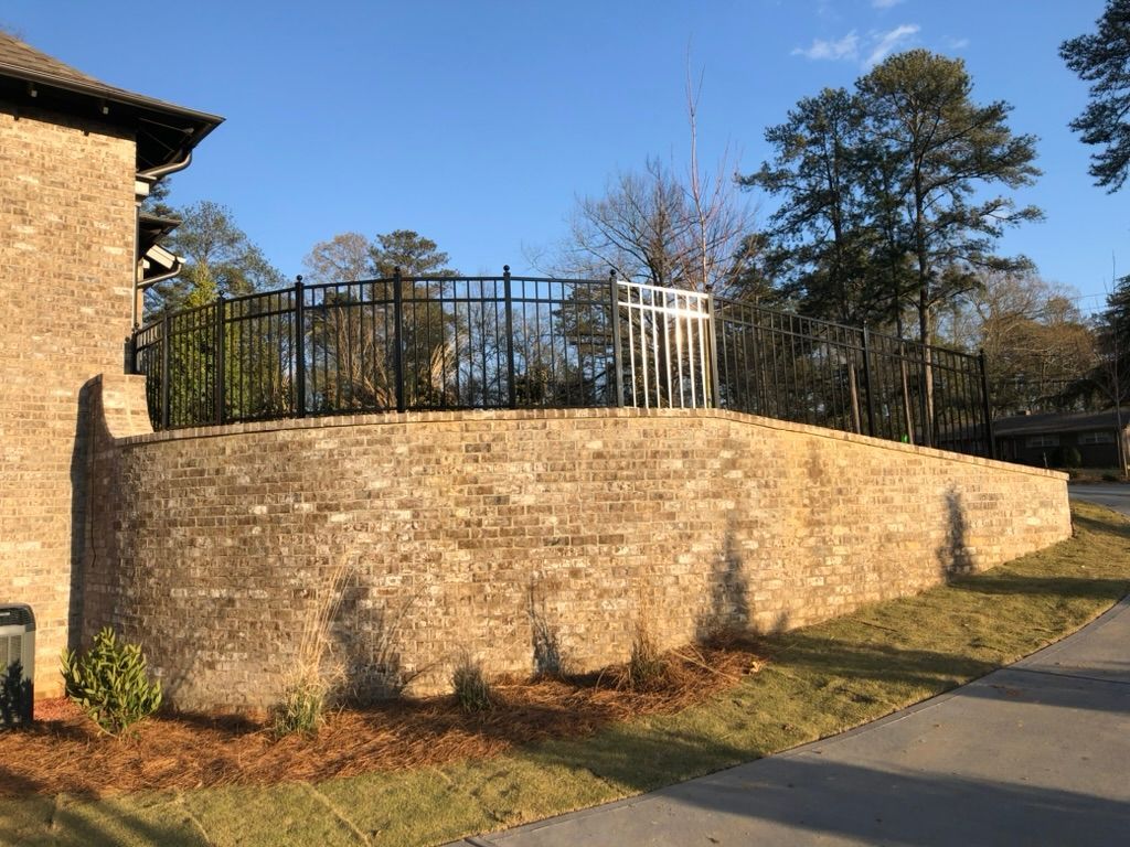 Brick retaining wall with black and white metal railing and a clear blue sky.