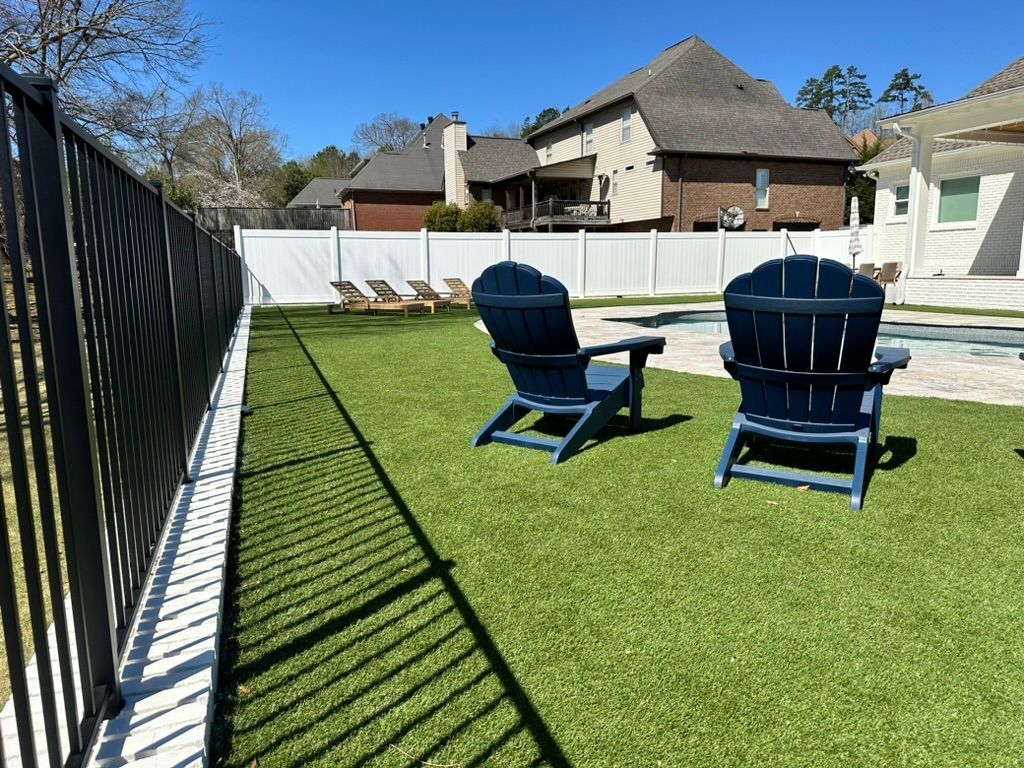 Backyard with blue chairs on green turf, black fence, white fence, and large house in the background.