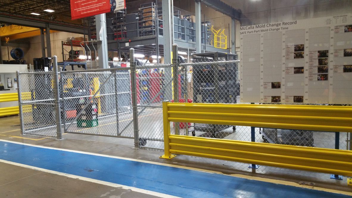Warehouse interior with chain link fence, yellow barriers, and equipment storage. Blue and gray floor.