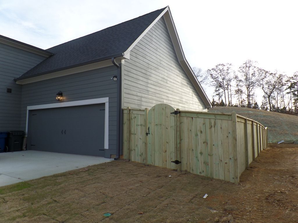 Gray house with gray garage door, and light wood fence. The fence has a gate.