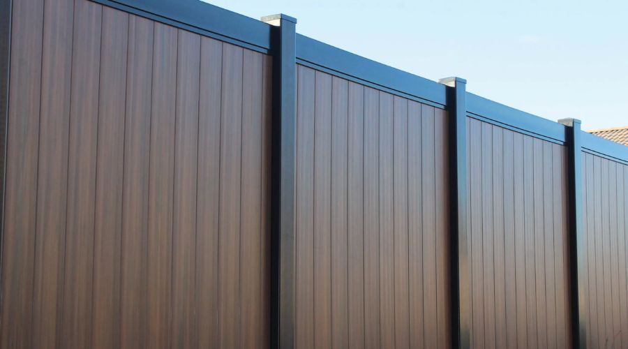 Tall dark wood-grain composite privacy fence with black metal posts against a clear blue sky.