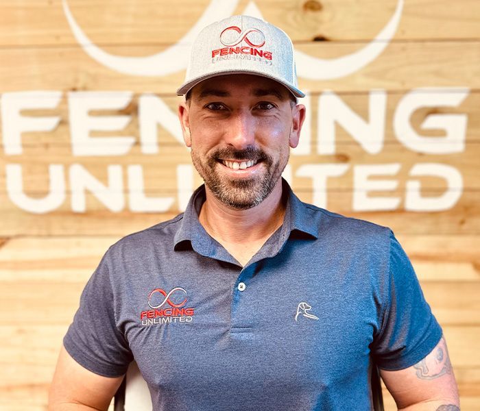 Man smiling, wearing a baseball cap and polo shirt in front of a wooden wall with