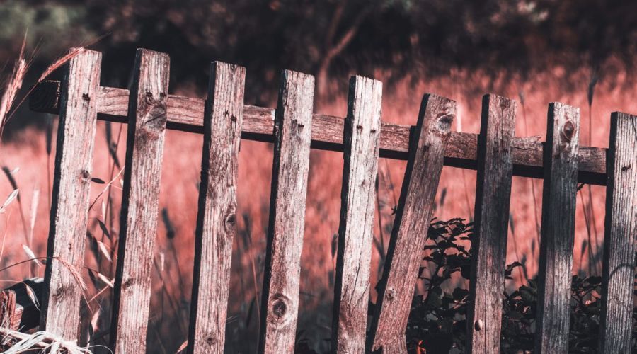 Old weathered wooden picket fence with broken and leaning pickets in need of repair.