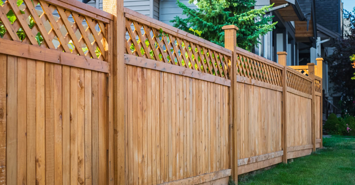 Wooden fence with lattice top, surrounding a grassy yard near a house.