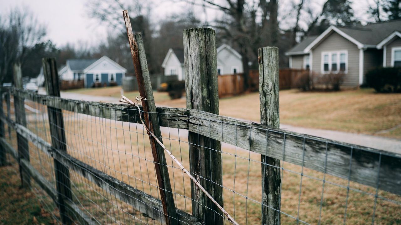 Weathered wooden fence in focus, houses and road in the blurred background.