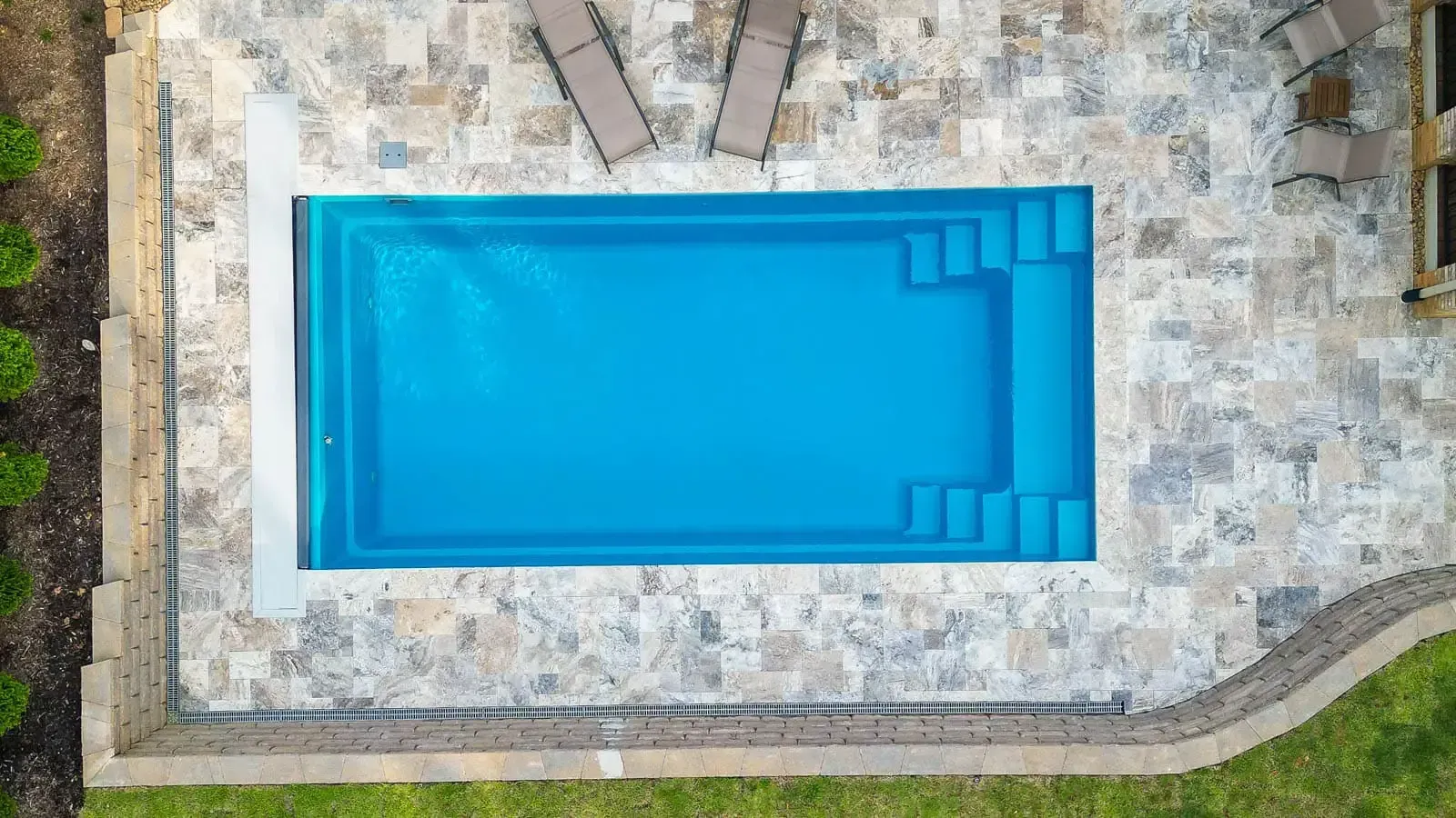 Aerial view of a rectangular blue swimming pool surrounded by stone paving and lounge chairs