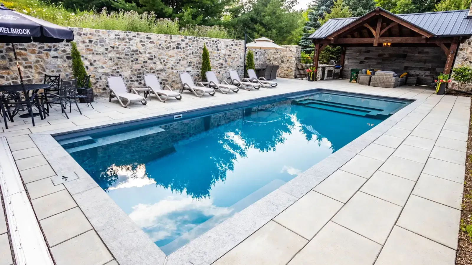 Rectangular outdoor pool with blue water, lounge chairs, and a stone patio beside a gazebo