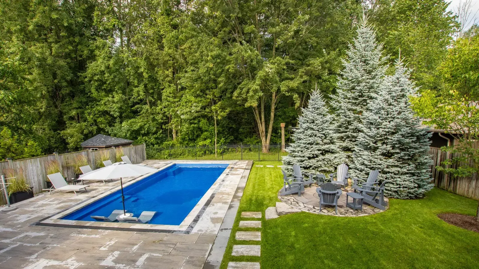 Backyard pool with lounge chairs, stone patio, and evergreen trees in the background