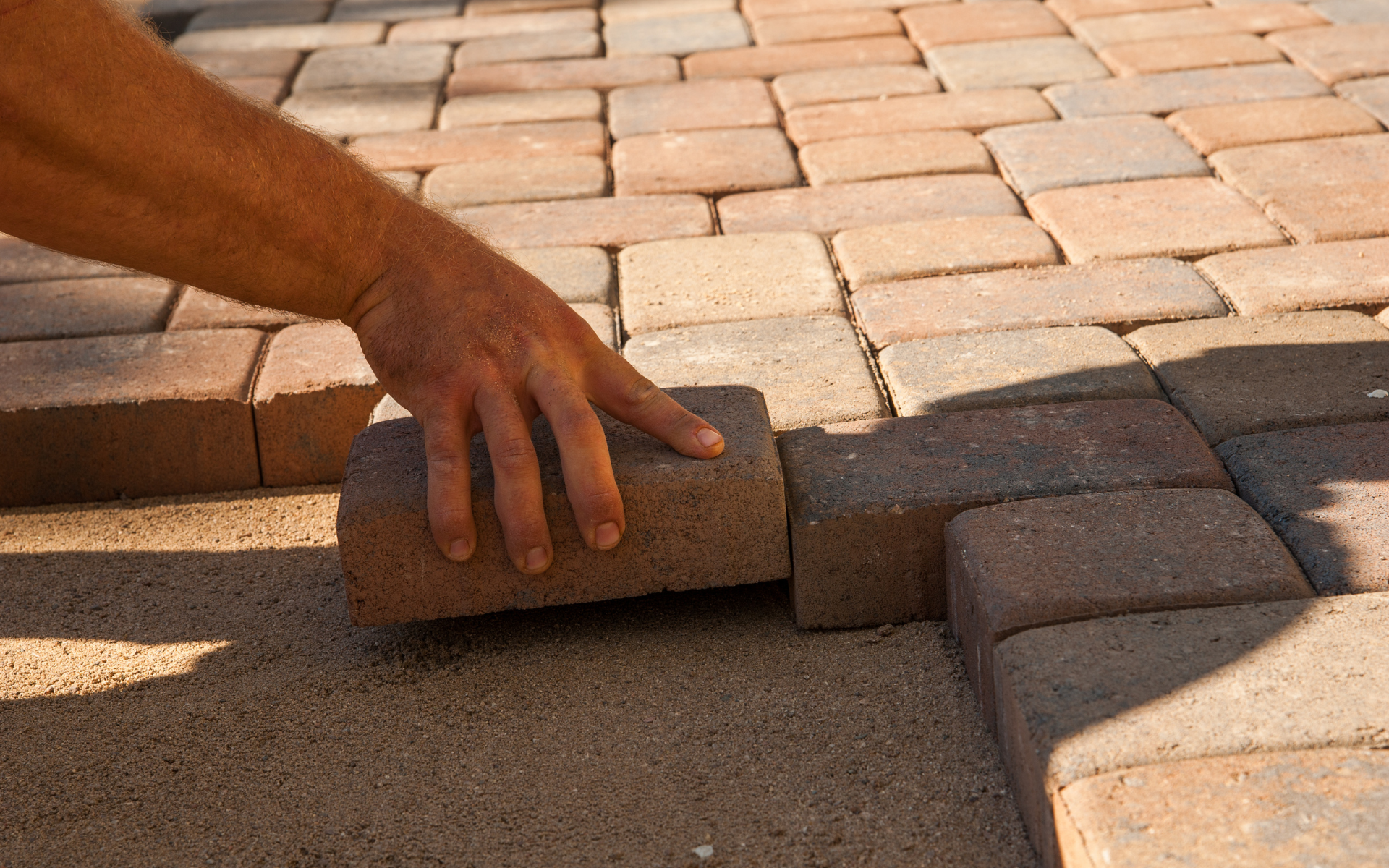 Hand placing a brick into a cobblestone driveway under construction