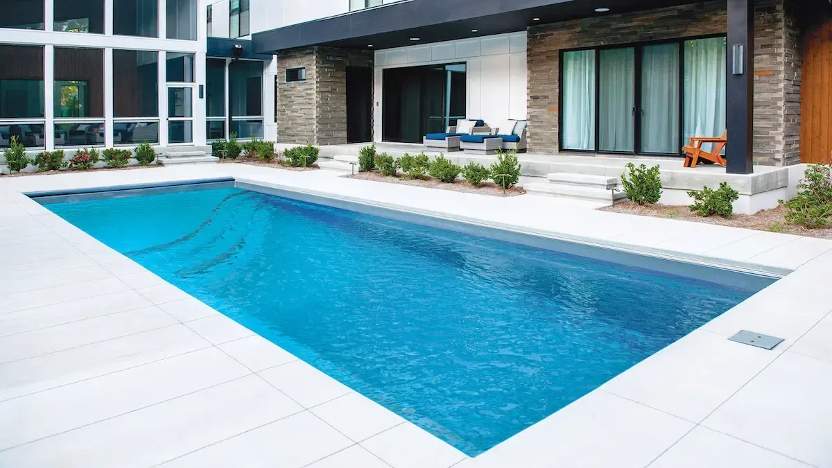 Modern backyard pool with blue water beside a contemporary house and patio seating