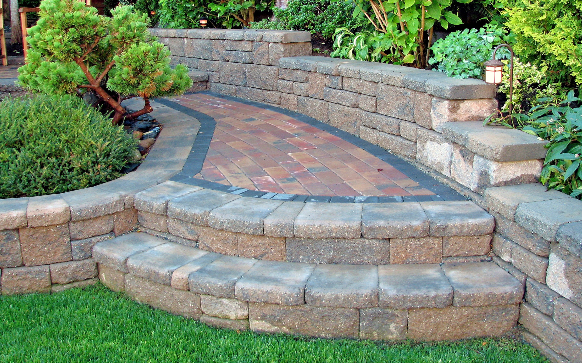 Curved stone garden steps with brick pavers, bordered by retaining walls and lush greenery