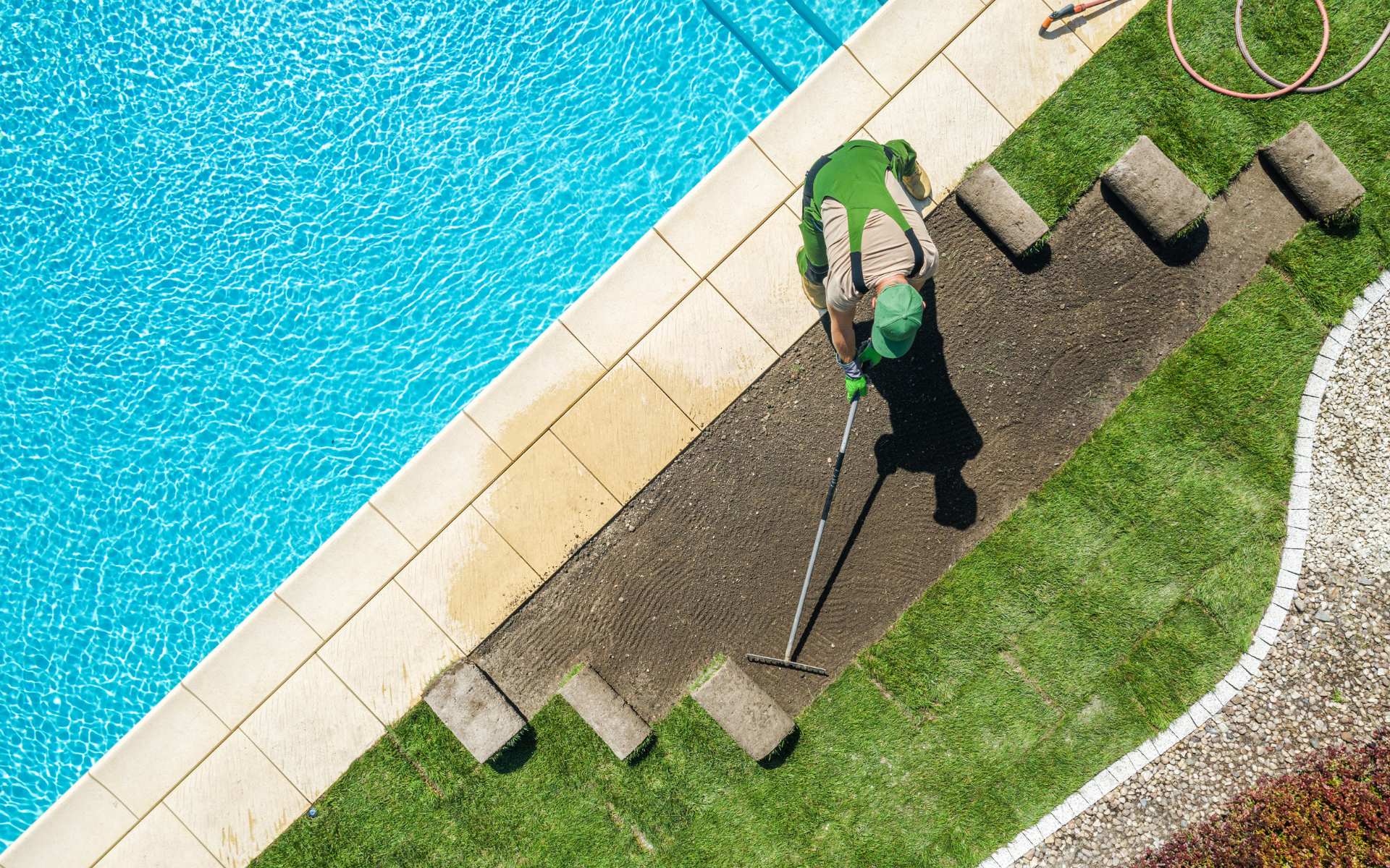 Person using a hose to water lawn beside a swimming pool