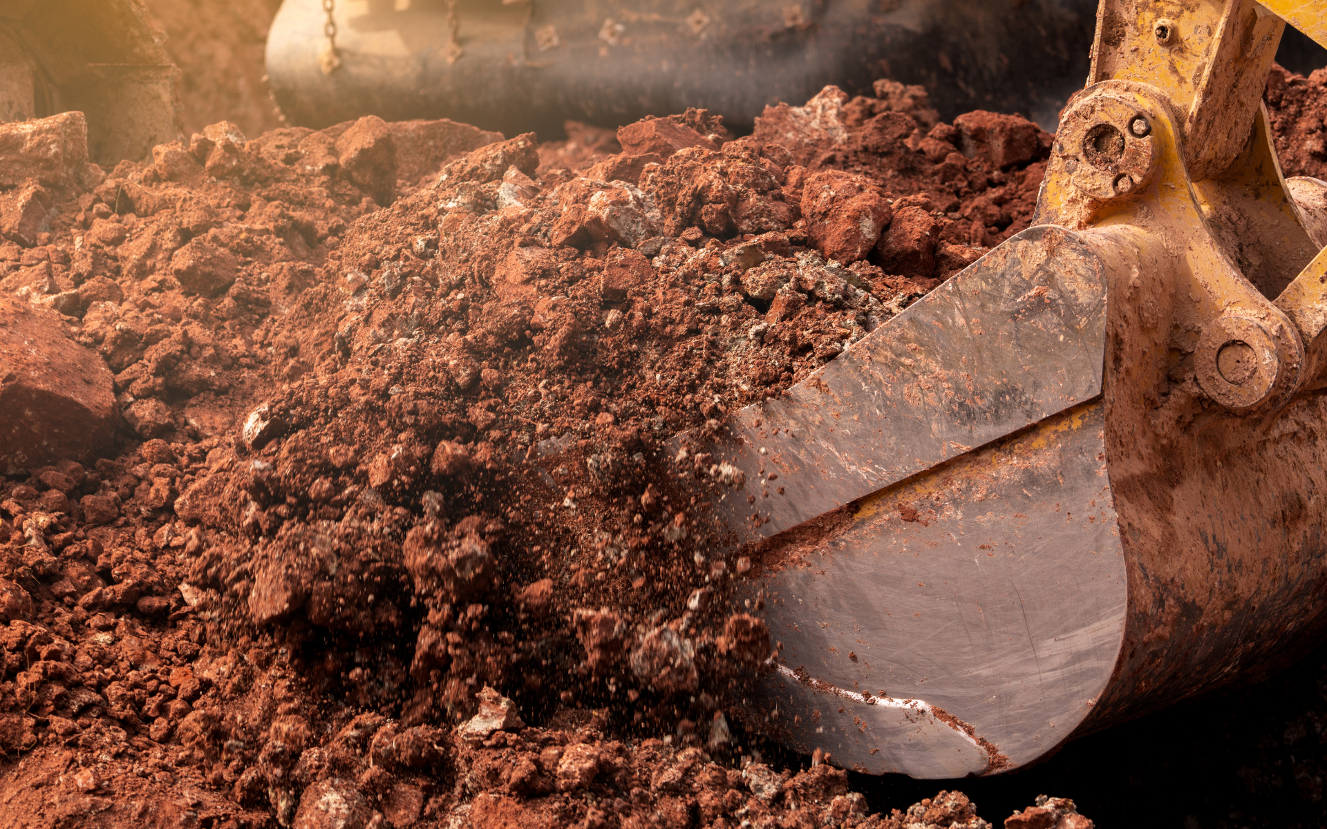 Excavator bucket scooping reddish dirt at a construction site