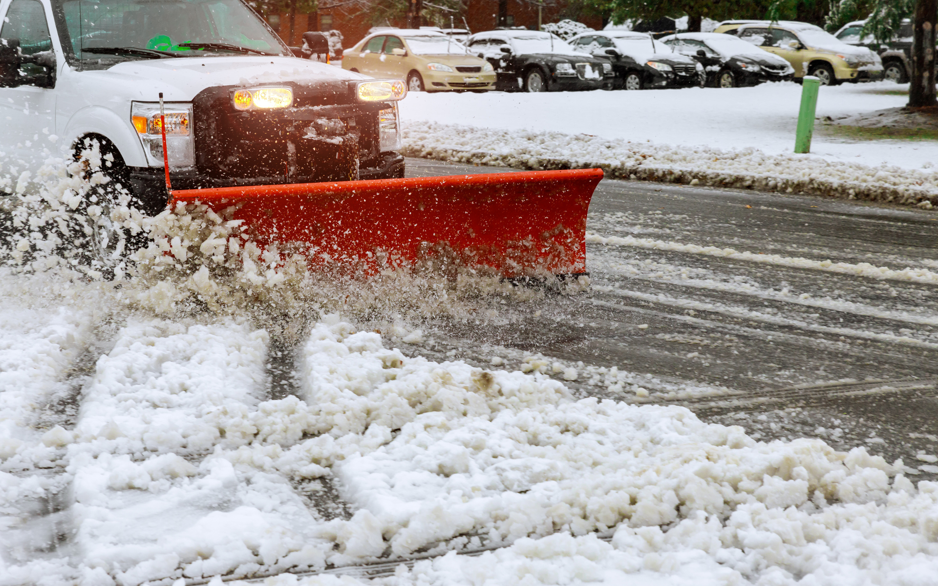 Snowplow clearing slushy snow on a snowy street, red plow blade pushing snow aside