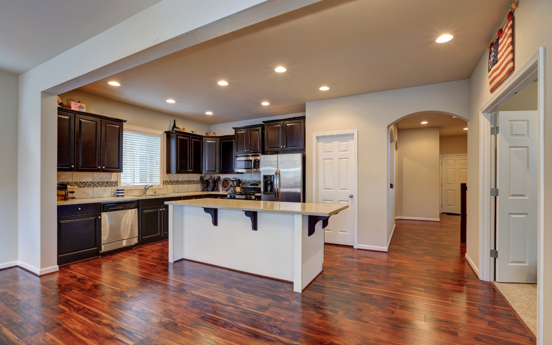 Modern open kitchen with dark wood cabinets, granite island, recessed lights, and hardwood floors