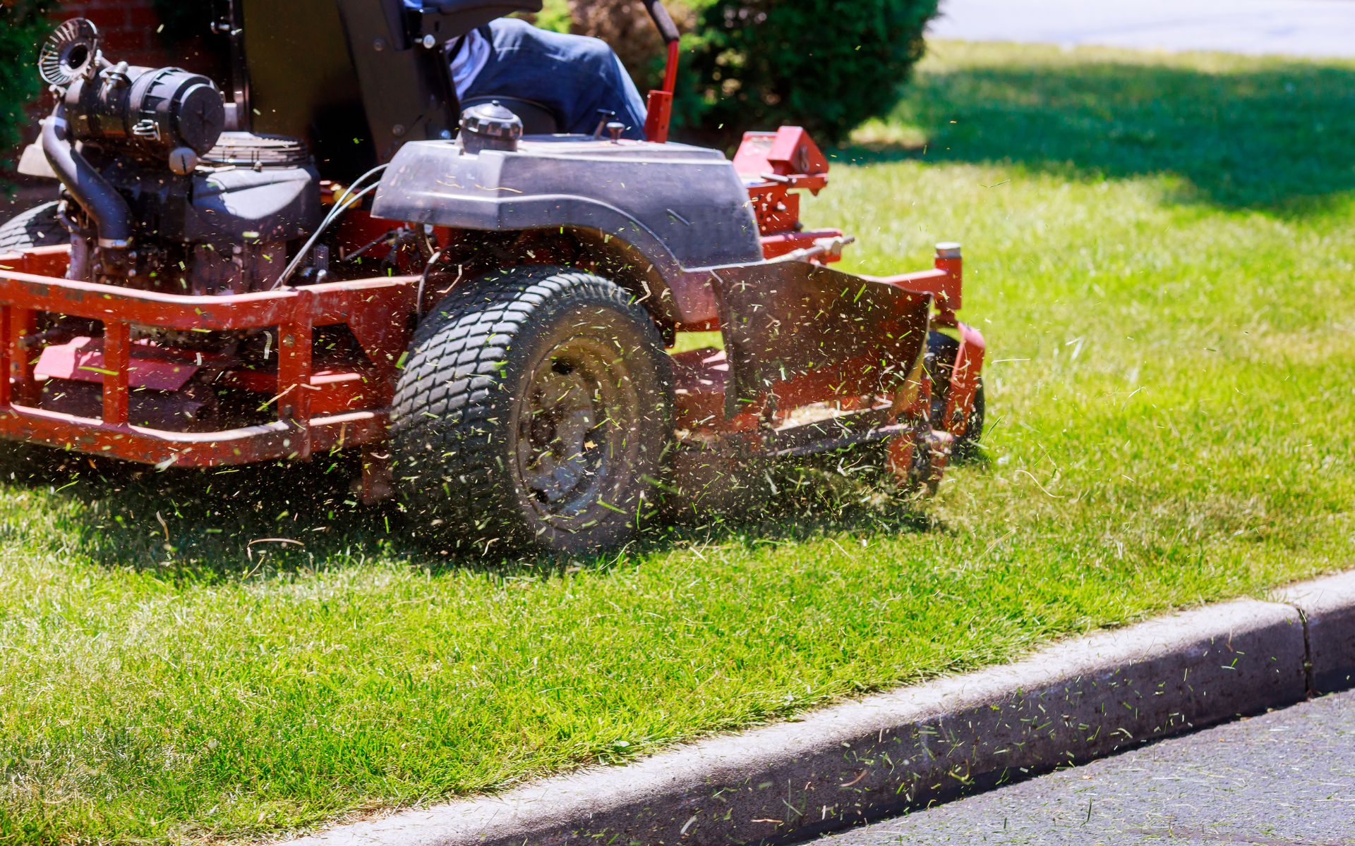 Red riding lawn mower mowing a green grassy lawn near a curb