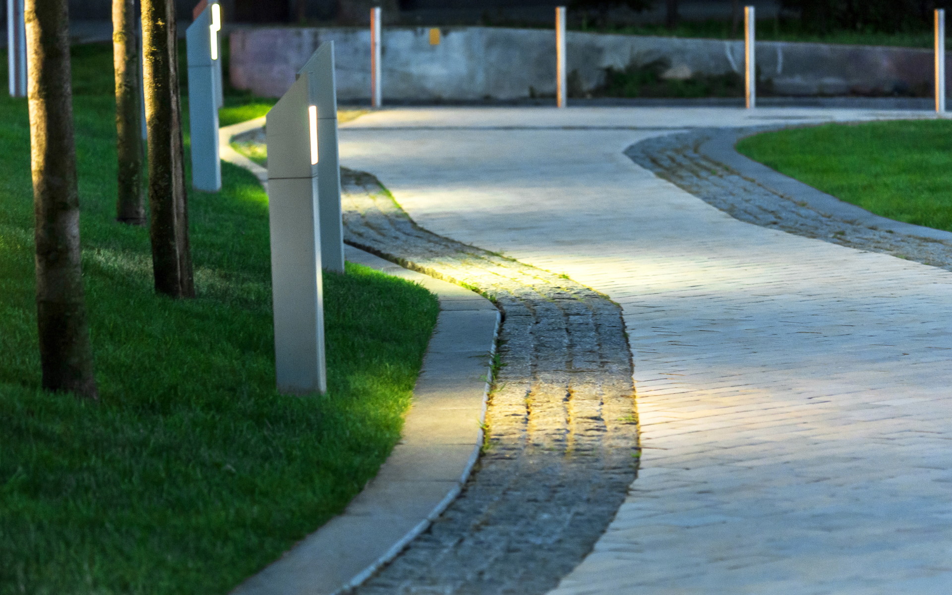Curved paved park path with a yellow tactile strip, bordered by grass and trees.