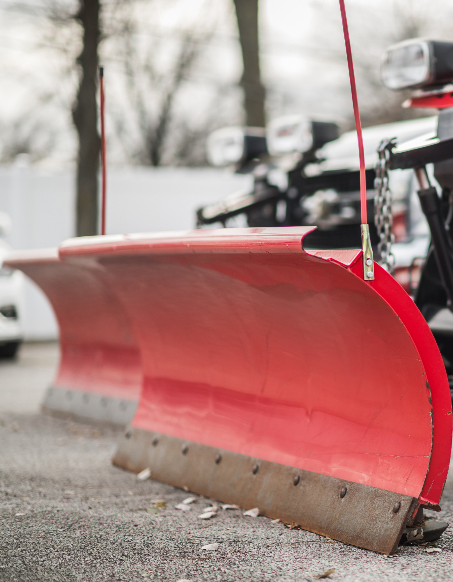 Red snow plow blade attached to a vehicle on a snowy roadside