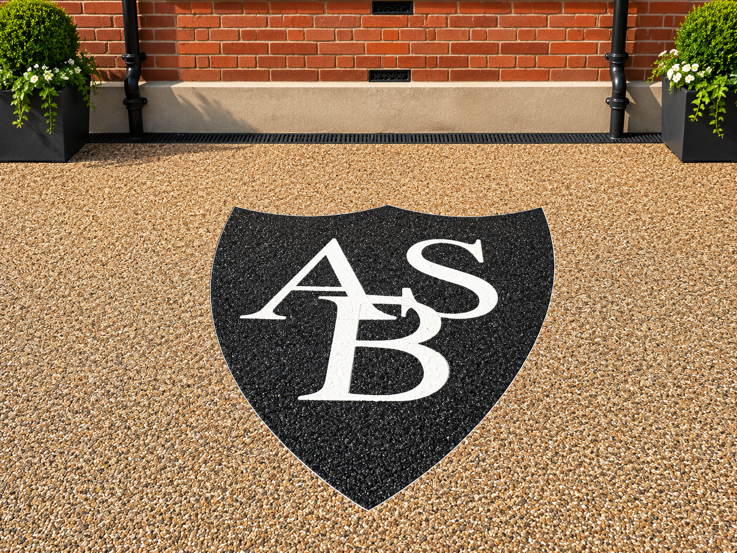Black shield logo with white “ASB” letters on a pebble driveway in front of a brick house.