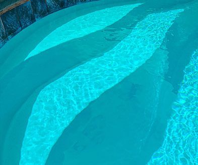Bright turquoise swimming pool water with sunlight reflections and curved shadows