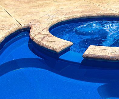 Curved swimming pool with bright blue water and tan stone deck