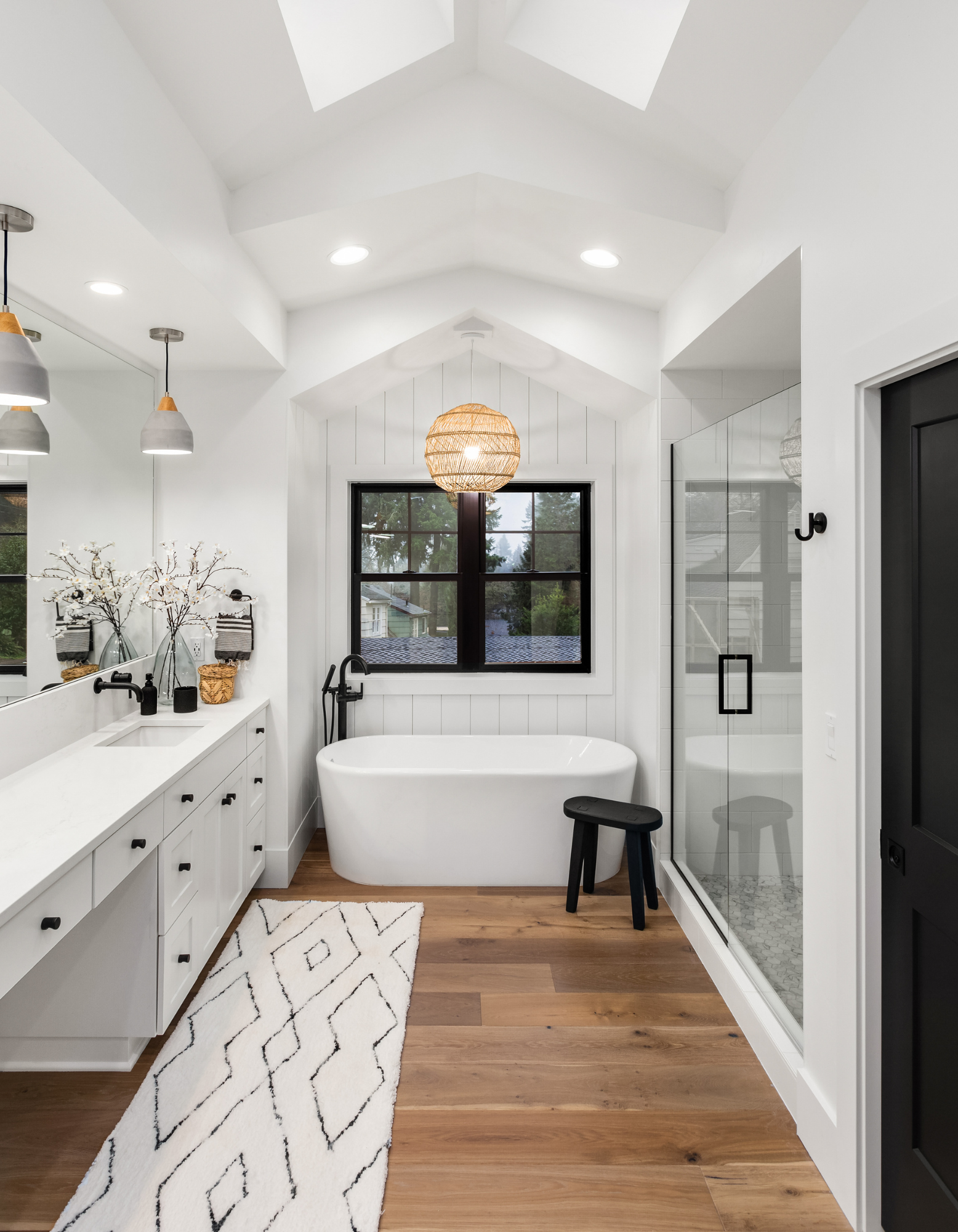 Bright modern bathroom with freestanding tub, glass shower, double vanity, skylights, and wood floor