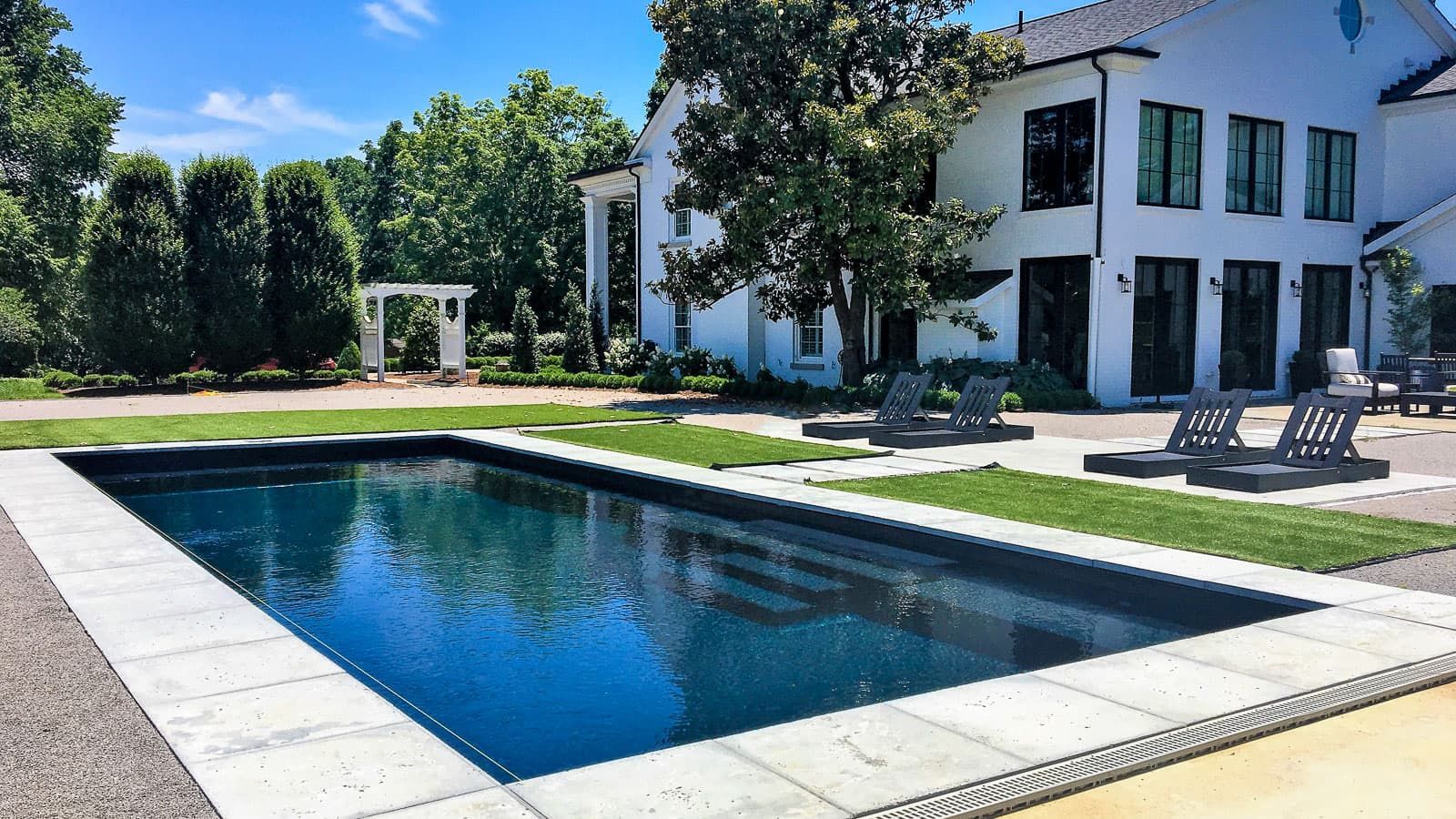 Modern house with a rectangular swimming pool in a sunny backyard garden