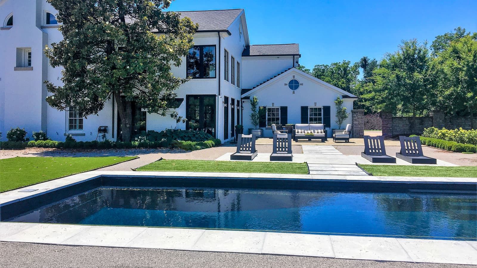 Modern white house with a backyard swimming pool and patio seating in bright daylight
