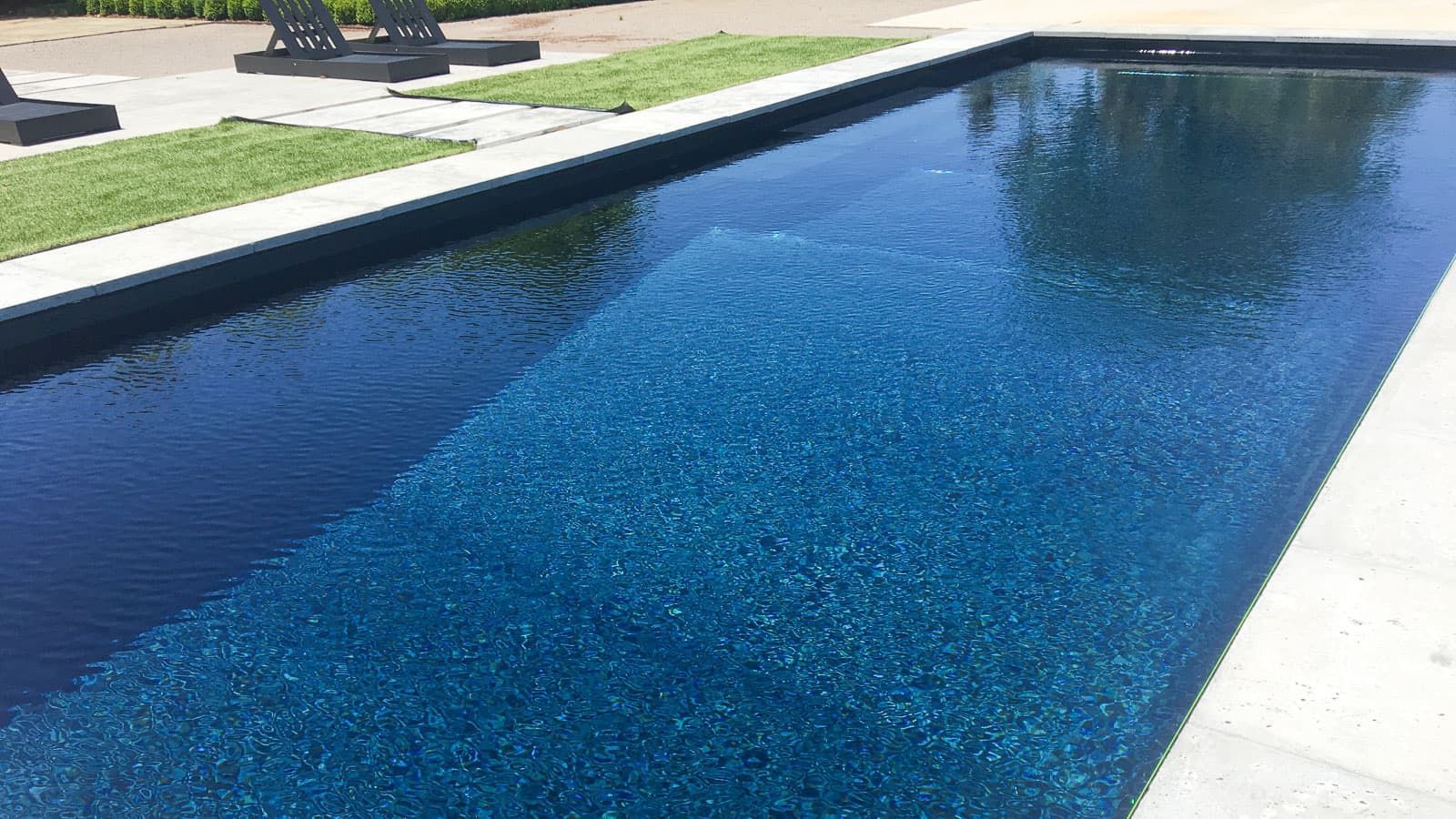 Long rectangular outdoor swimming pool with blue water and white stone edges
