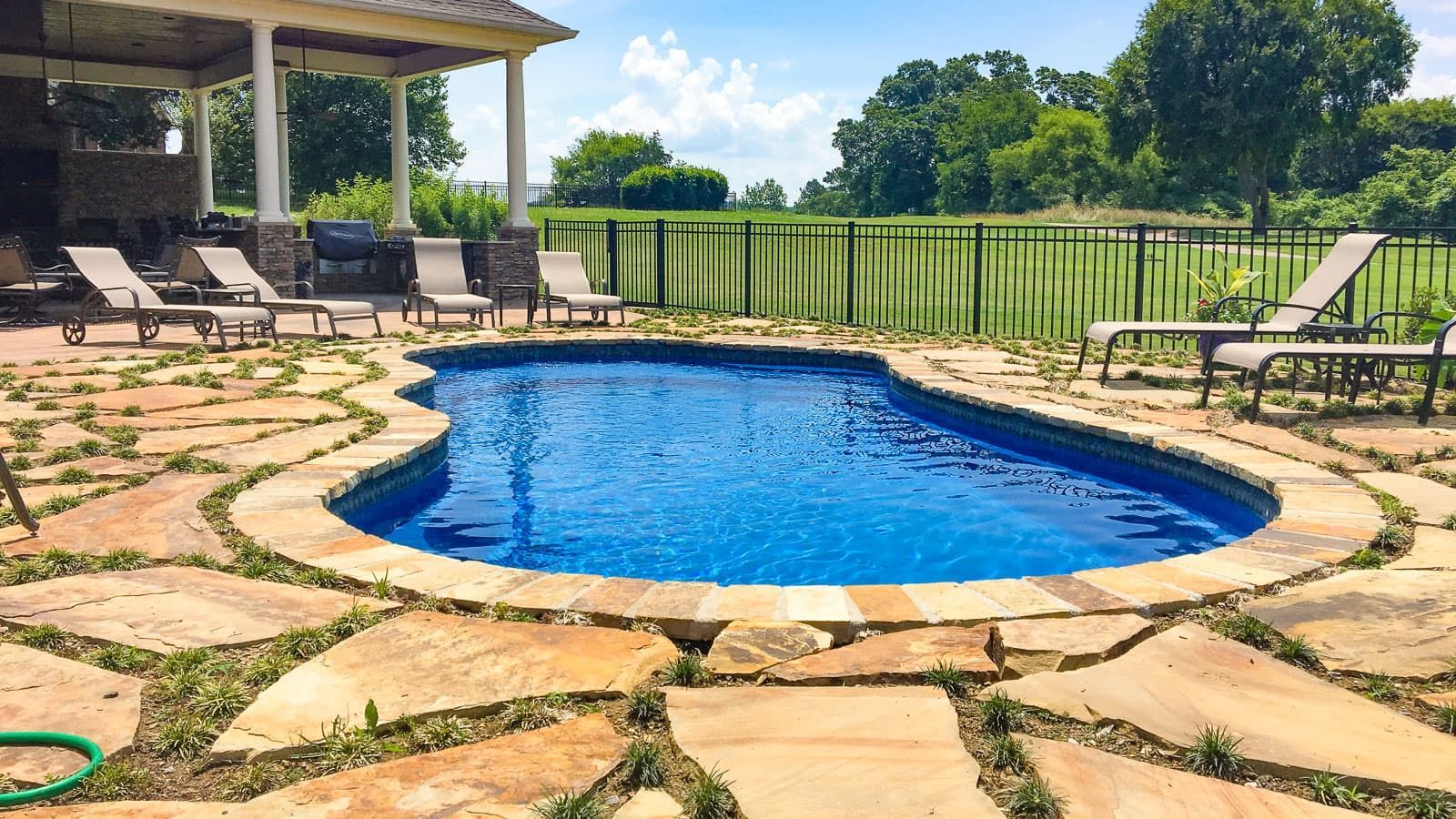 Blue backyard pool with stone patio, lounge chairs, and green lawn under a covered porch