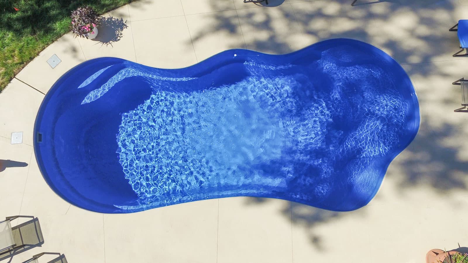 Blue kidney-shaped swimming pool seen from above with rippling water and surrounding patio area