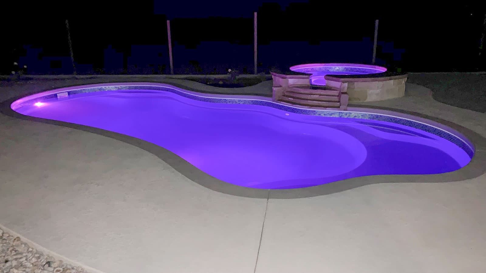 Backyard swimming pool glowing purple at night with a curved slide and stone spa