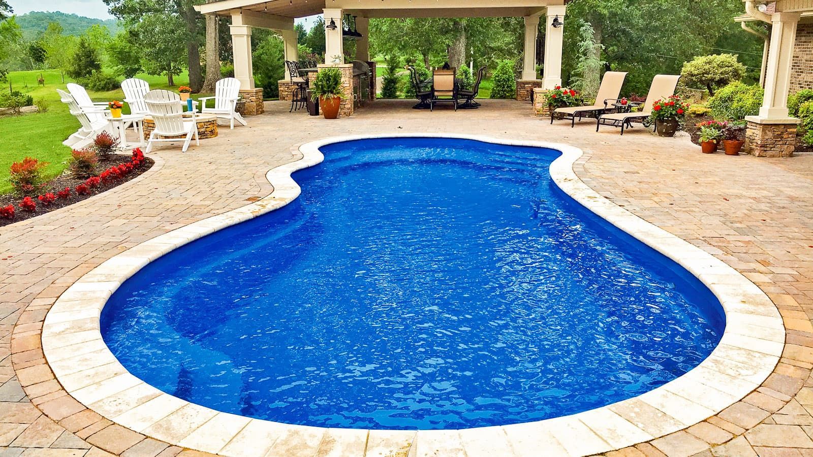 Blue kidney-shaped swimming pool on a stone patio with lounge chairs and greenery around it