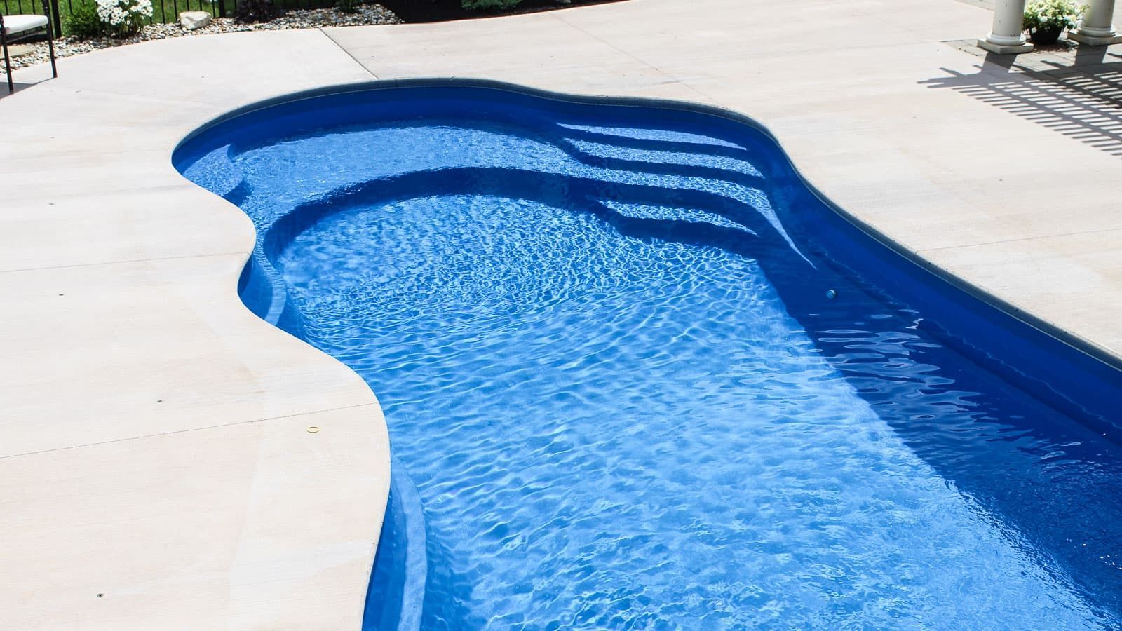 Curved blue swimming pool with light concrete deck outdoors