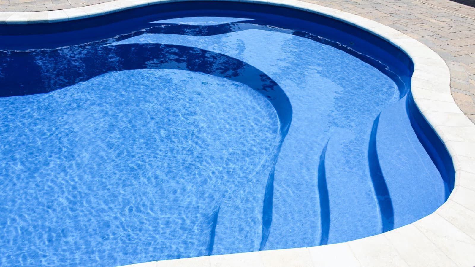 Blue swimming pool with curved white coping and shallow steps on the right