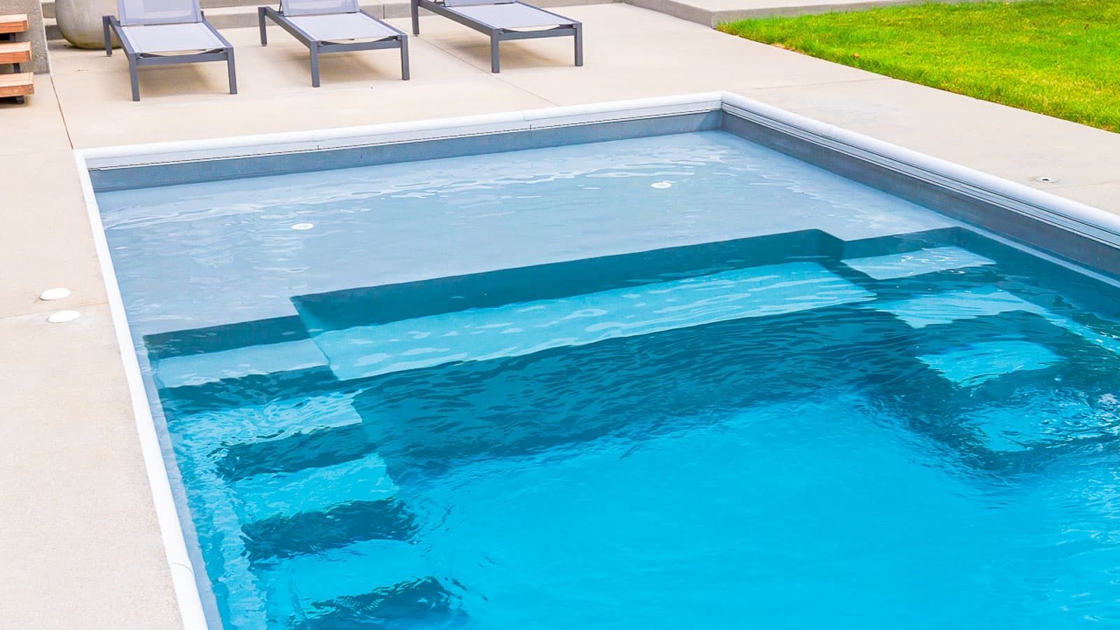 Rectangular backyard pool with clear blue water and lounge chairs on the deck