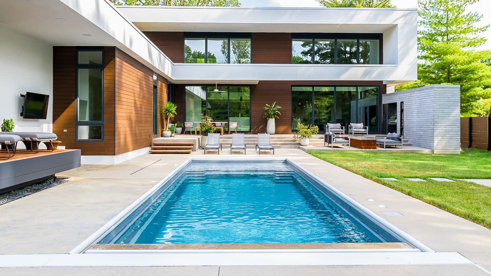 Modern house with a backyard pool, patio seating, and green lawn