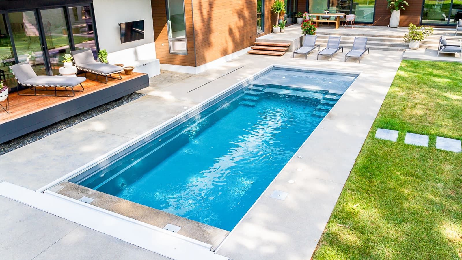 Modern backyard with a rectangular blue swimming pool beside a patio and lounge chairs