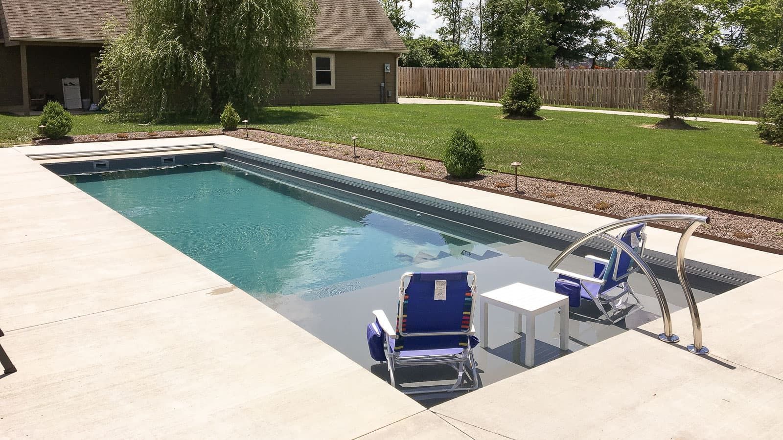 Backyard pool with two lounge chairs and a small table on the deck