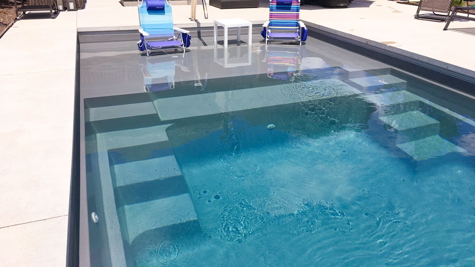 Modern backyard pool with blue water and two lounge chairs on the deck