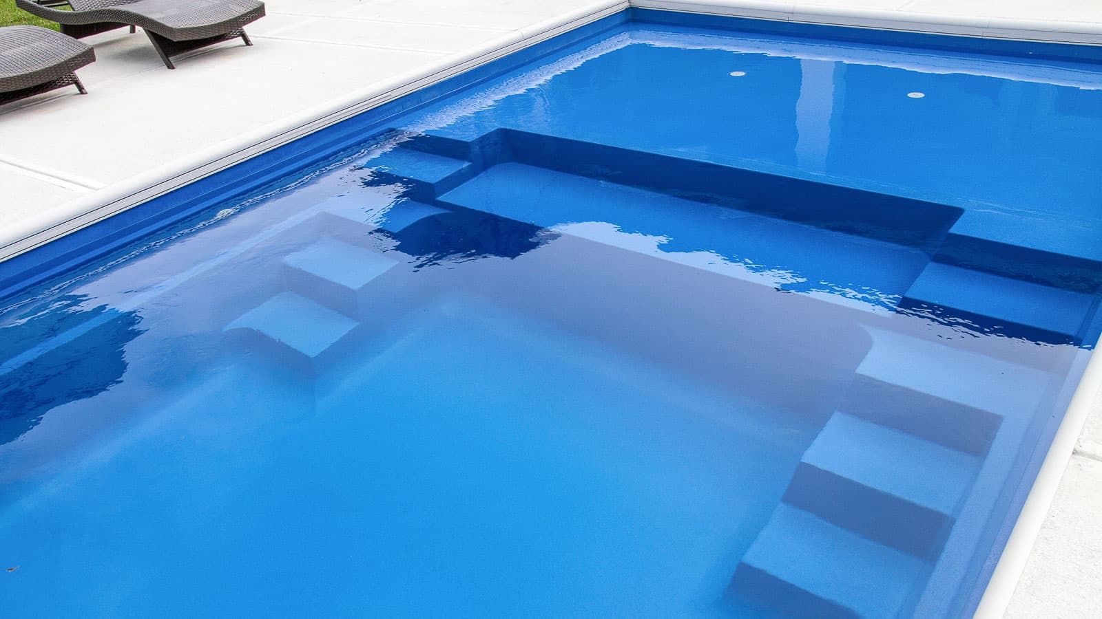 Blue swimming pool with submerged steps and white pool deck