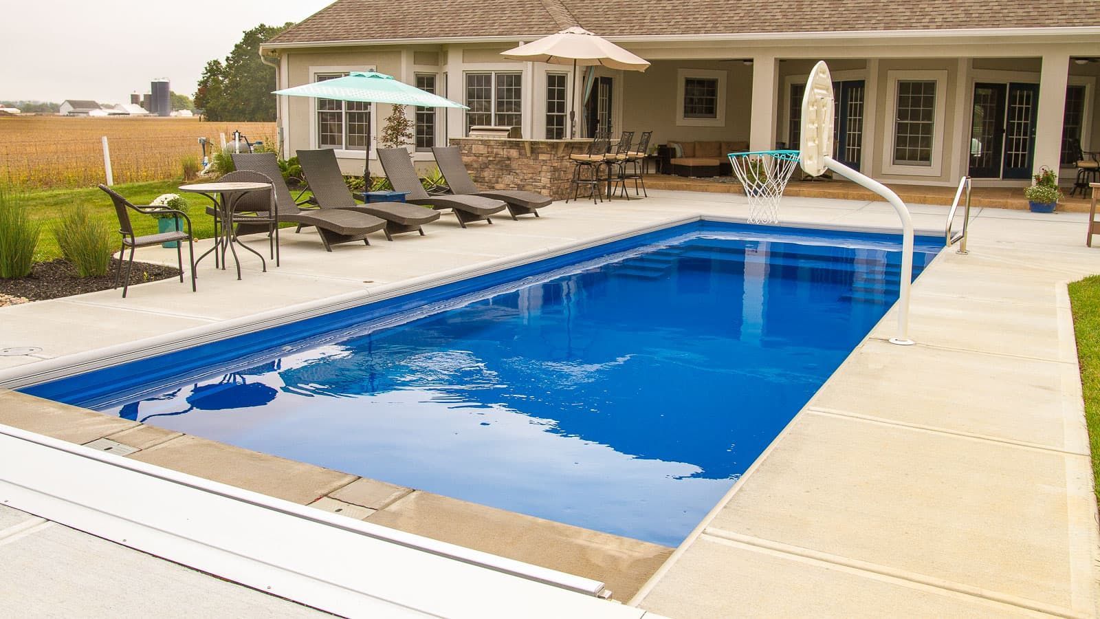 Backyard swimming pool with patio chairs, umbrellas, and a house in the background