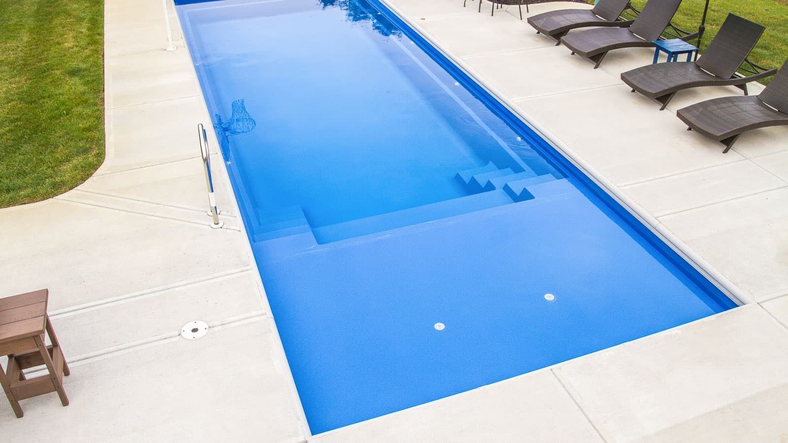 Long narrow blue swimming pool beside white deck chairs on a patio