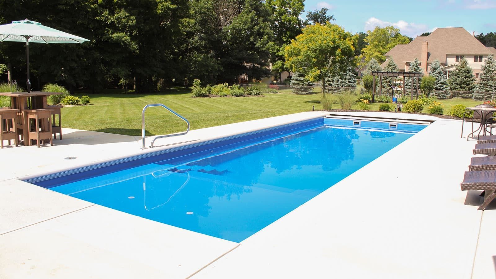 Backyard swimming pool with blue water, white deck, and patio furniture on a sunny day