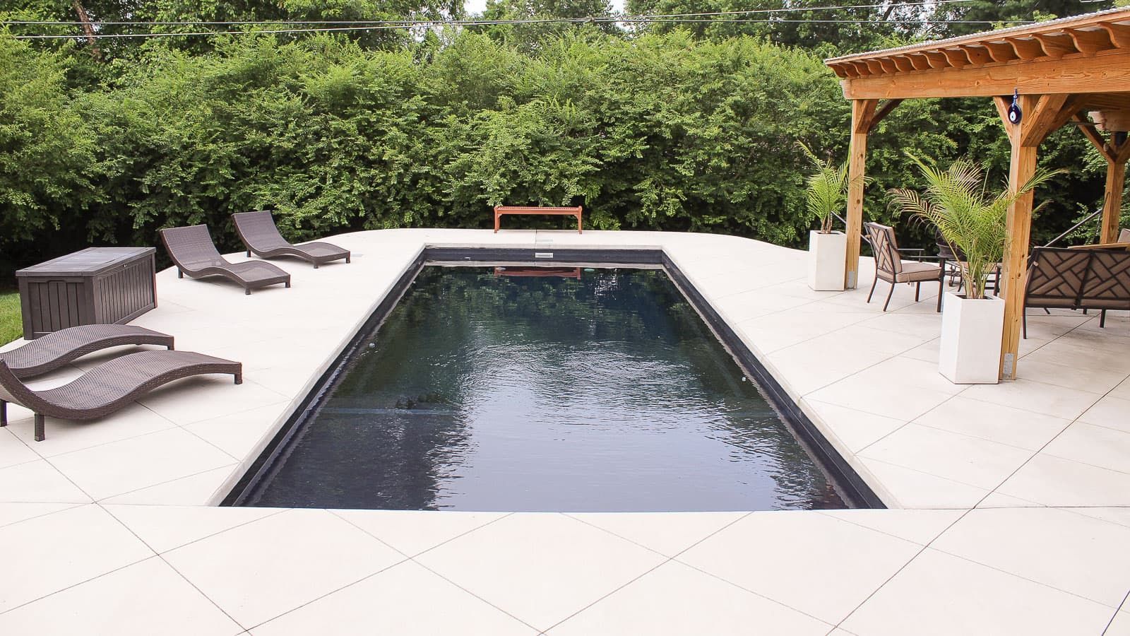 Backyard pool surrounded by lounge chairs, greenery, and a wooden pergola
