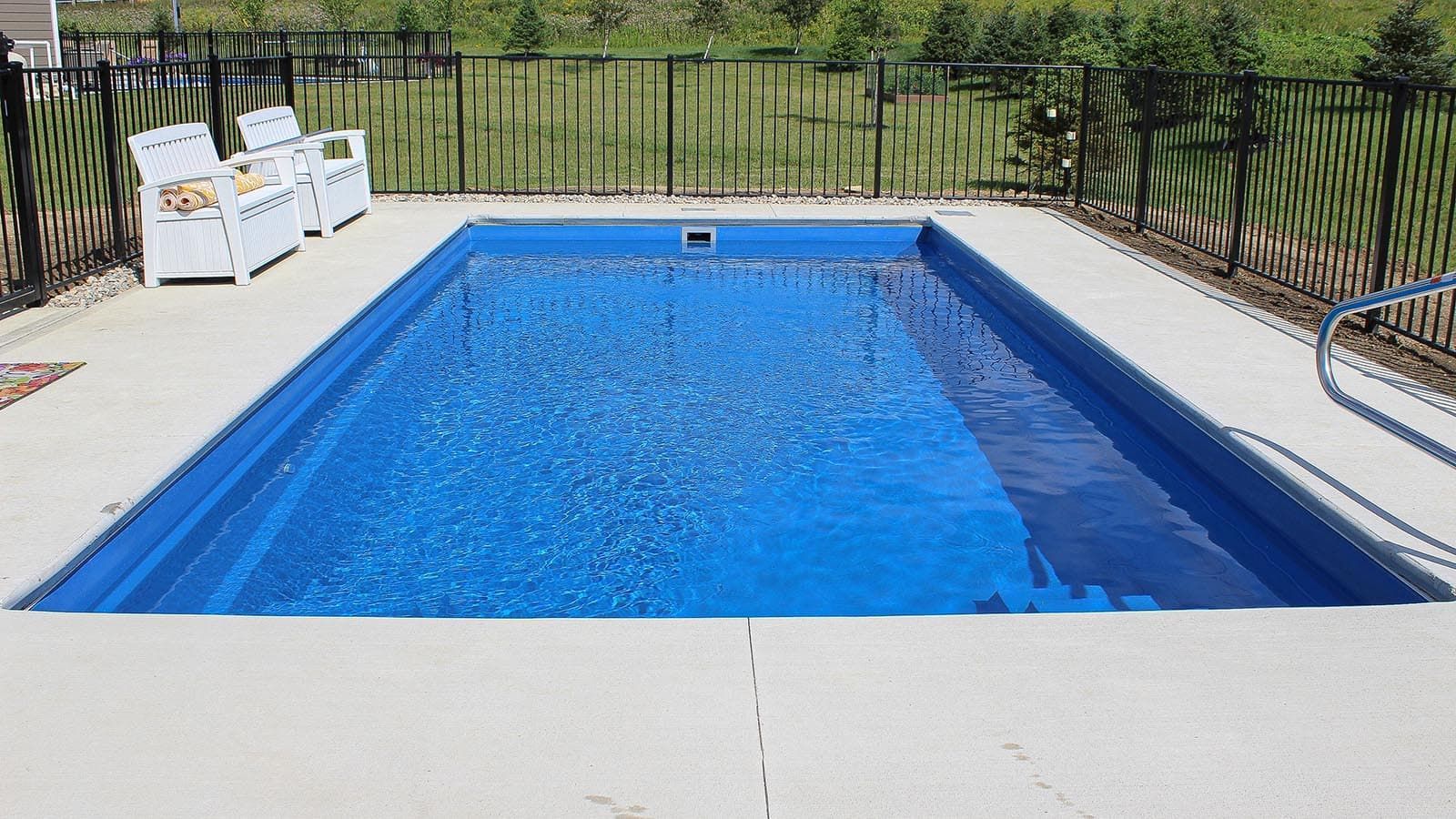 Backyard swimming pool with bright blue water, white deck, and black fence surrounding it