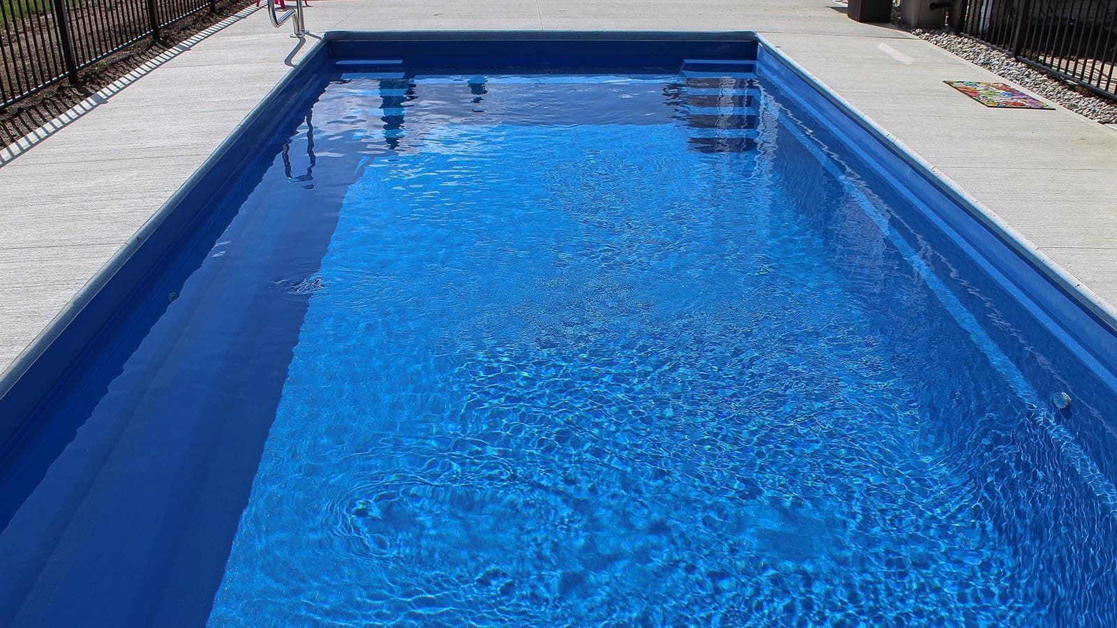 Blue rectangular swimming pool with calm water, viewed from the shallow end on a sunny day