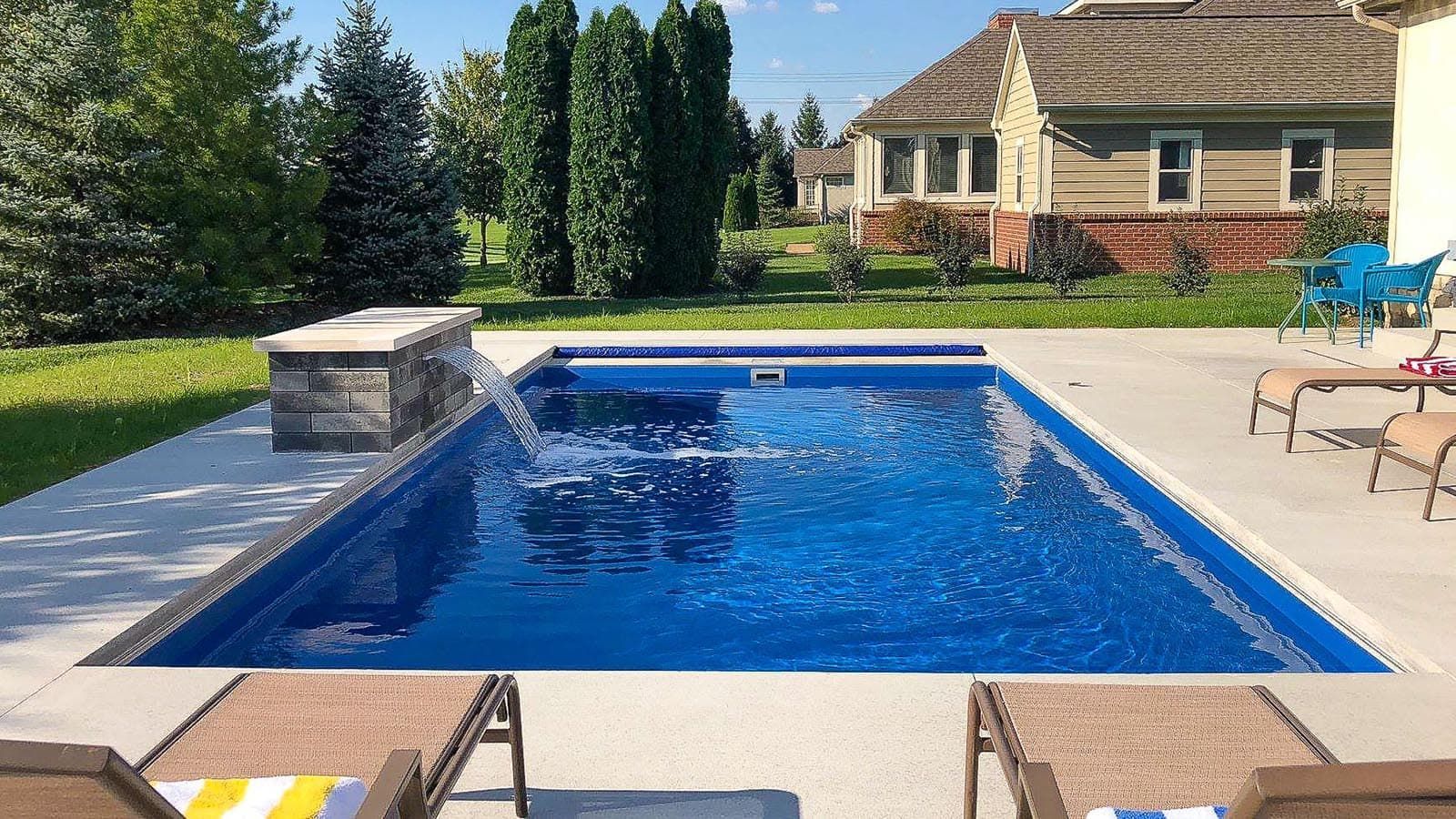 Backyard swimming pool with blue water, lounge chairs, and a house in the background